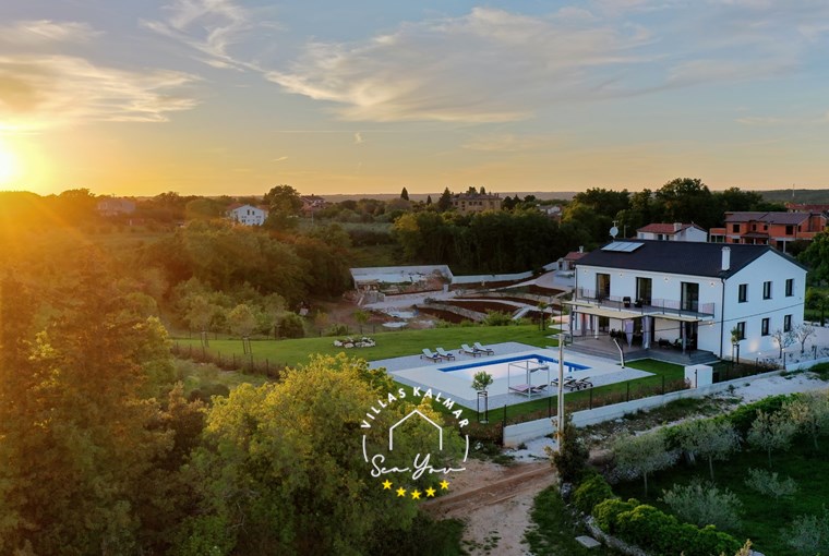 Zalazak sunca iznad šume pored moderne vile s privatnim bazenom i vrtom