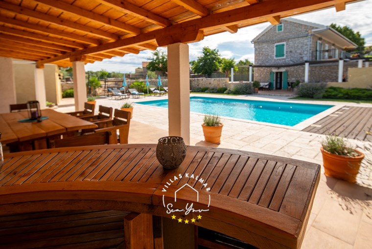 Covered outdoor dining area with view over the private pool and renovated stone Villa Bozini Dvori, near Zadar