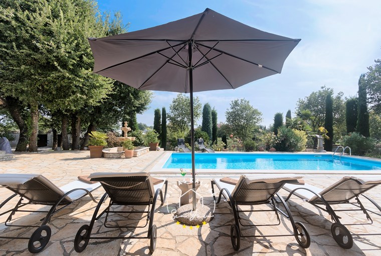 Ležaljke, suncobran i drveće pored bazena u vili